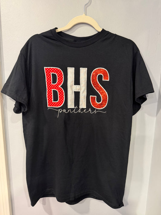 A black short-sleeve t-shirt hanging on a wooden hanger against a light gray wall. The shirt features a large graphic on the front with the letters 'BHS' in red and white, with 'panthers' written in white script underneath.