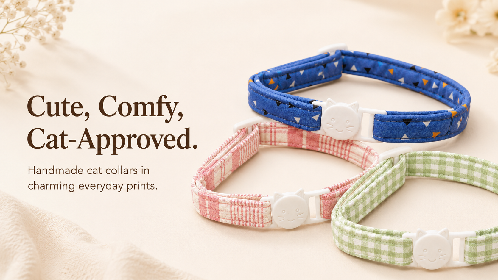Three handmade cat collars in different prints are displayed on a soft beige fabric background with decorative dried flowers. The collars feature blue with tiny geometric patterns, pink gingham, and green gingham.